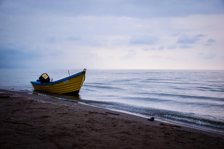 a yellow and blue boat sitting on top of a beach, a photo, pexels contest winner, romanticism, overcast dawn, black sea, a cozy, a single