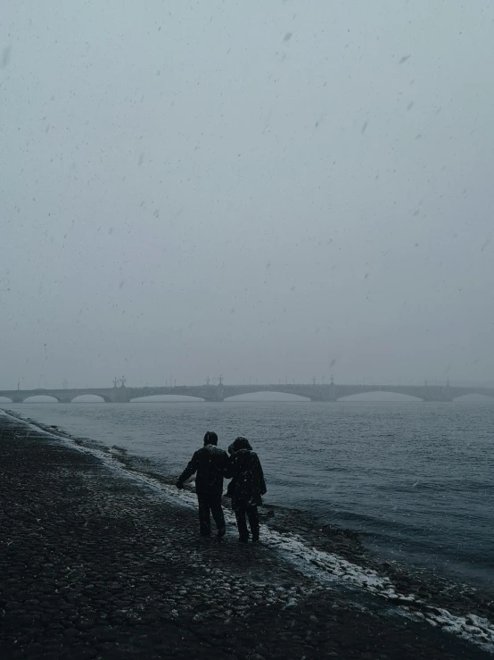 a couple of people standing on top of a beach, pexels contest winner, snowing outside, river confluence, reykjavik junior college, bridge