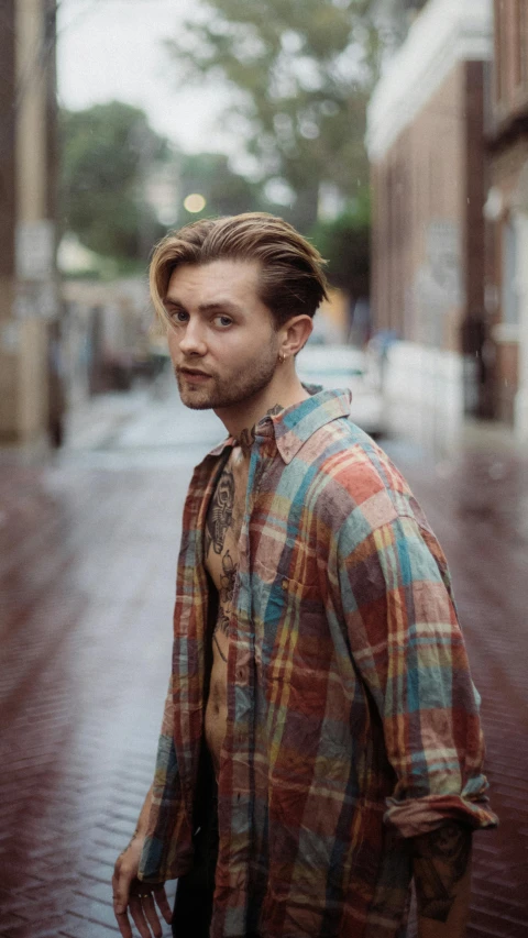 a man standing in the middle of a city street, an album cover, by Drew Tucker, pexels contest winner, renaissance, wearing a plaid shirt, long swept back blond hair, faded out colors, actor