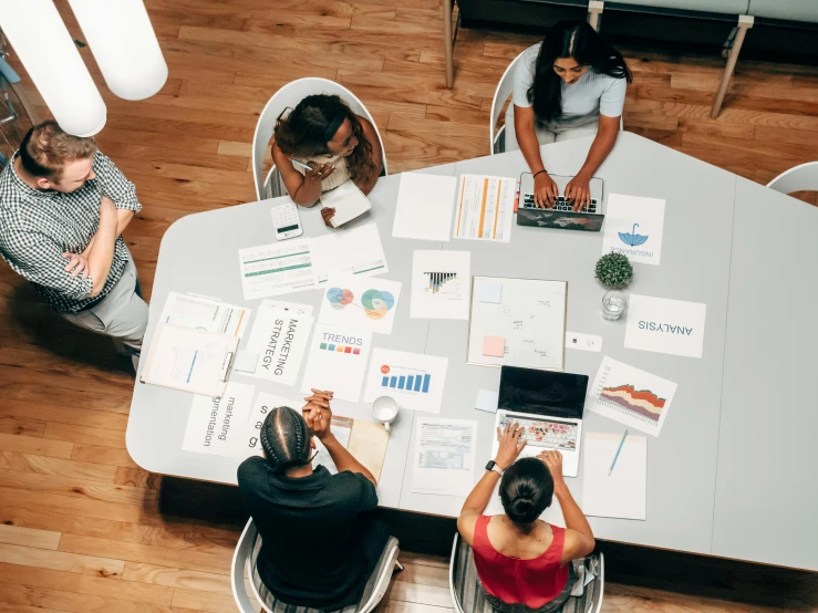 a group of people sitting around a table with laptops, pexels contest winner, process art, 9 9 designs, wide high angle view, papers on table, charts