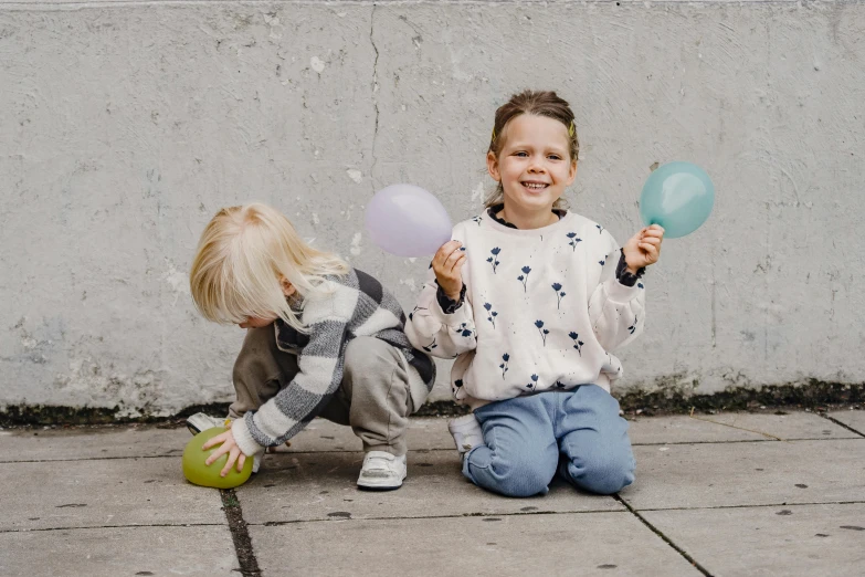a couple of kids sitting on the ground with balloons, by Emma Andijewska, pexels contest winner, on the concrete ground, 4yr old, sirius a and sirius b, activity play centre
