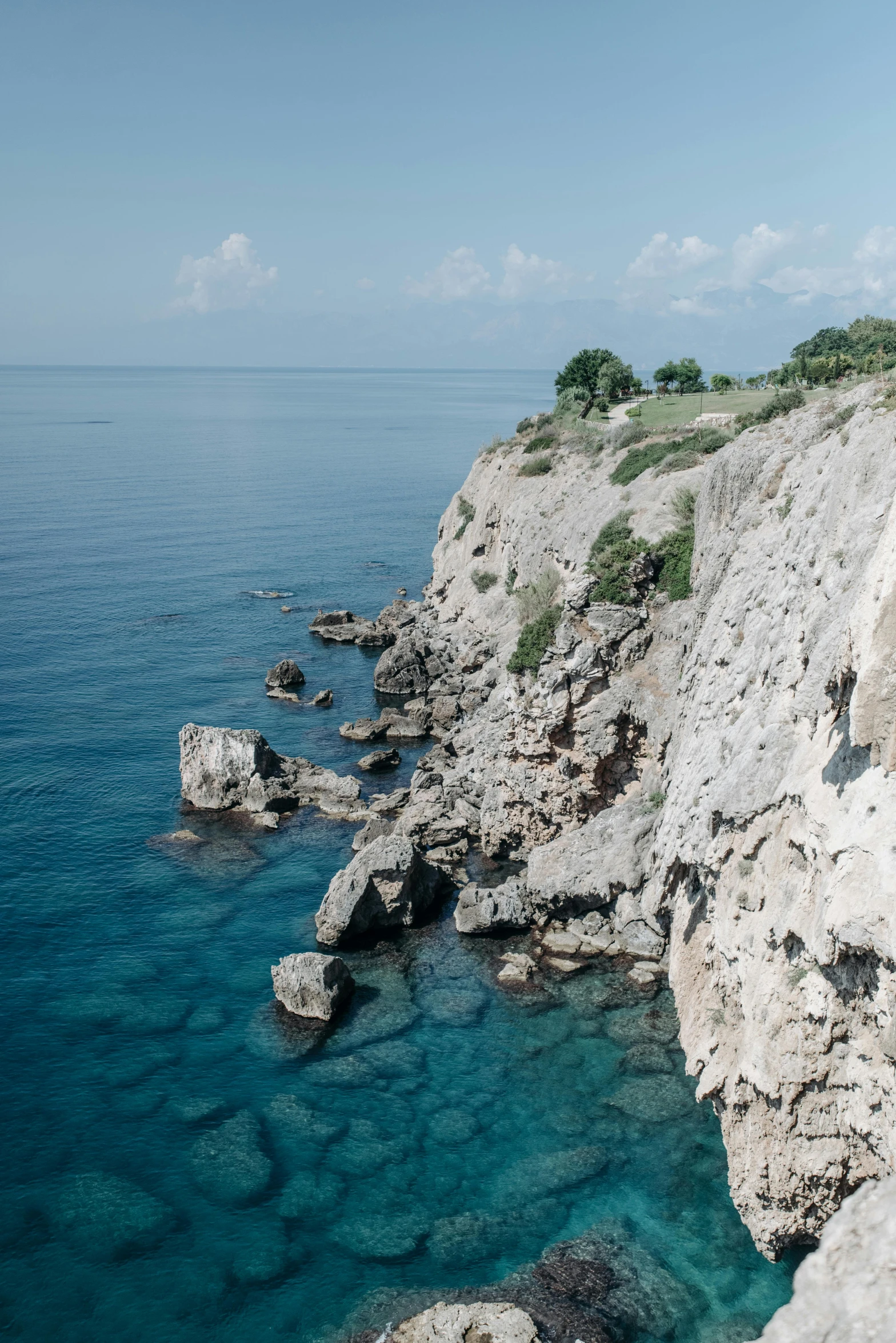 a man standing on top of a cliff next to the ocean, a picture, inspired by Constantine Andreou, unsplash, romanticism, crystal clear blue water, rock walls, ehime, panoramic shot