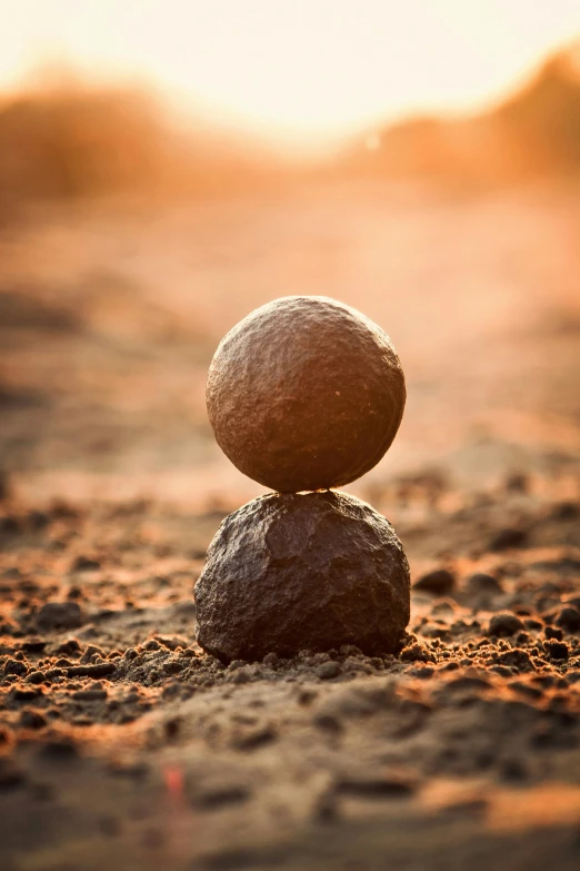 two rocks stacked on top of each other in the sand, an album cover, unsplash, land art, sphere, iron giant at sunset, macro focus, single figure