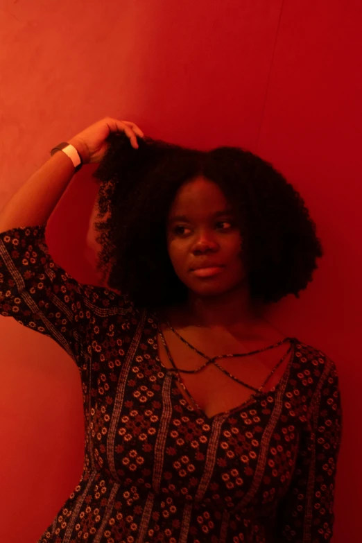 a woman standing in front of a red wall, an album cover, natural hair, shot at dark with studio lights, low quality photograph, threatening pose