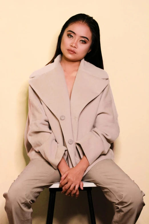 a woman sitting on top of a stool, an album cover, by Robbie Trevino, trending on pexels, light brown coat, young asian girl, thick collar, 15081959 21121991 01012000 4k