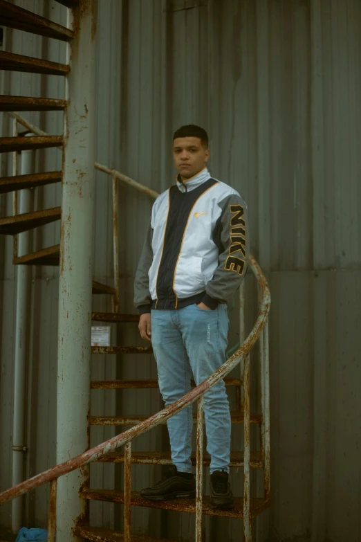 a man standing in front of a spiral staircase, an album cover, inspired by Jordan Grimmer, unsplash, renaissance, wearing a jeans jackets, wearing a track suit, male teenager, confident stance