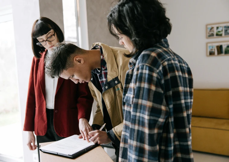 a group of people standing around a table, pexels contest winner, academic art, writing on a clipboard, casually dressed, te pae, varying ethnicities