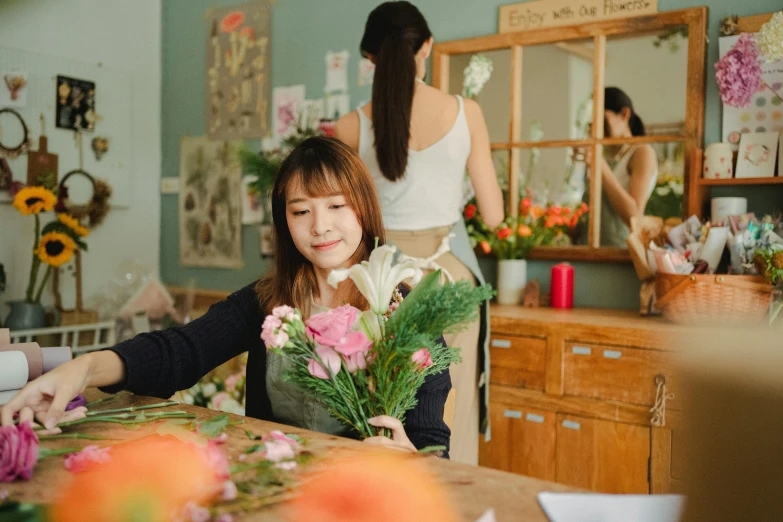 a woman sitting at a table with a bunch of flowers, pexels contest winner, arts and crafts movement, korean girl, people at work, woman holding another woman, fresh