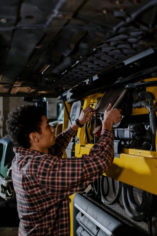 a man working on a vehicle in a garage, yellow and black trim, thumbnail, farming, mechanical engineering