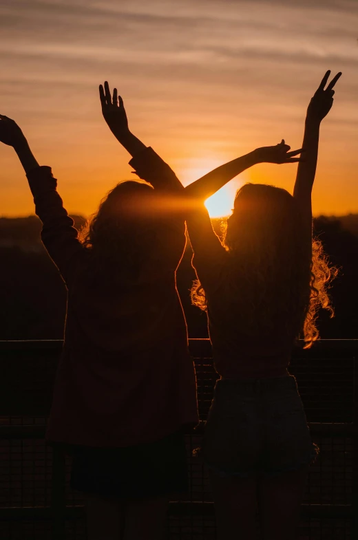 two women standing in front of a sunset, pexels contest winner, happening, hands in the air, college girls, two suns, rooftop party