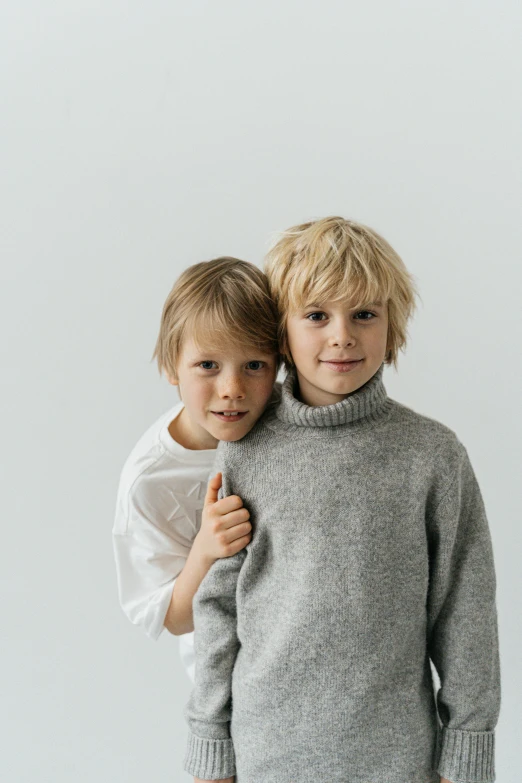 two young boys standing next to each other, light grey, wearing sweater, bedhead, medium - shot