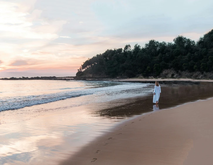 a woman standing on top of a beach next to the ocean, inspired by Pierre Puvis de Chavannes, unsplash, renaissance, australian beach, at gentle dawn pink light, long flowing white robe, ultrawide image