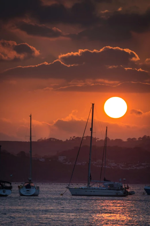 a group of sailboats floating on top of a body of water, by Peter Churcher, pexels contest winner, big red sun, cornwall, paul barson, sunset warm spring