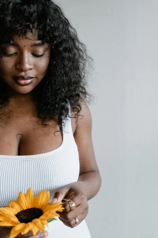 a woman in a white tank top holding a sunflower, trending on unsplash, dark complexion, with large breasts, dark. no text, perky woman made of petals