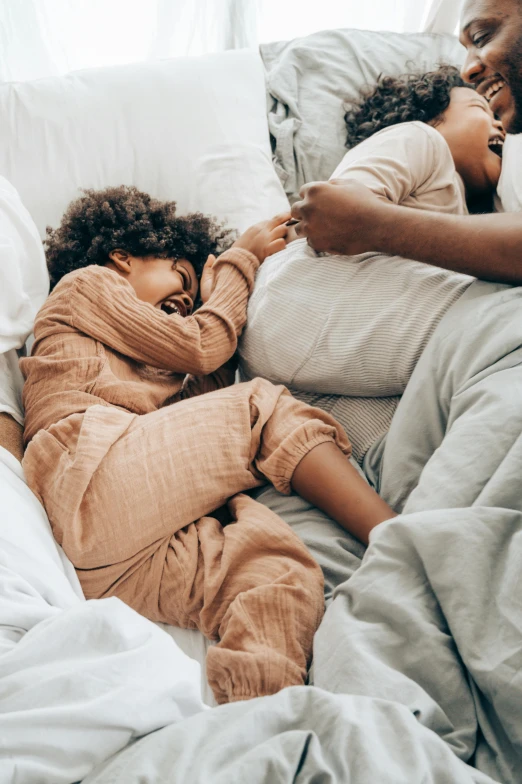 a man and woman laying in bed next to each other, by Matija Jama, pexels contest winner, with a kid, sleepwear, warm hues, diverse