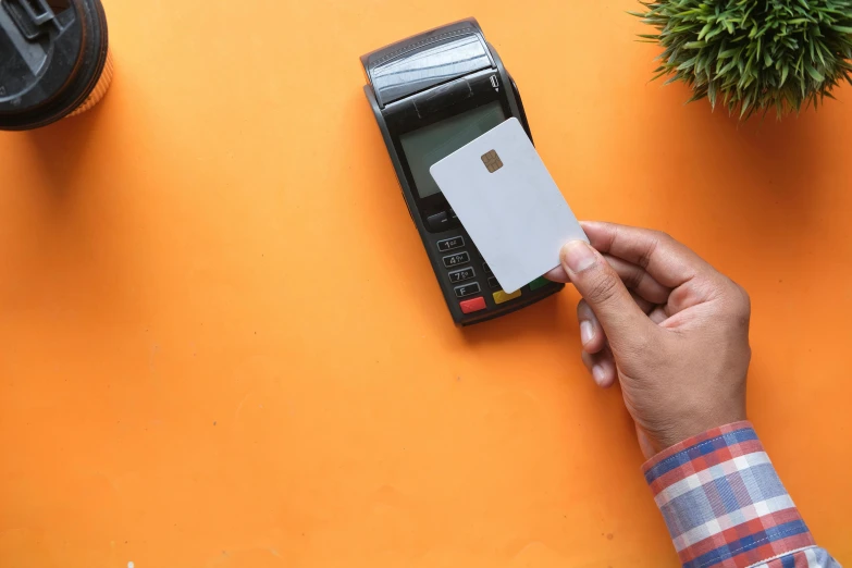 a person holding a credit card in front of a calculator, an album cover, pexels contest winner, private press, in front of an orange background, square, no - text no - logo, visa pour l'image