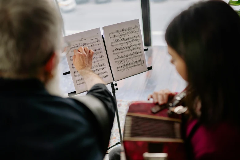 a man and a woman playing music in front of a window, unsplash, manuscript, conductor, sydney hanson, teaching