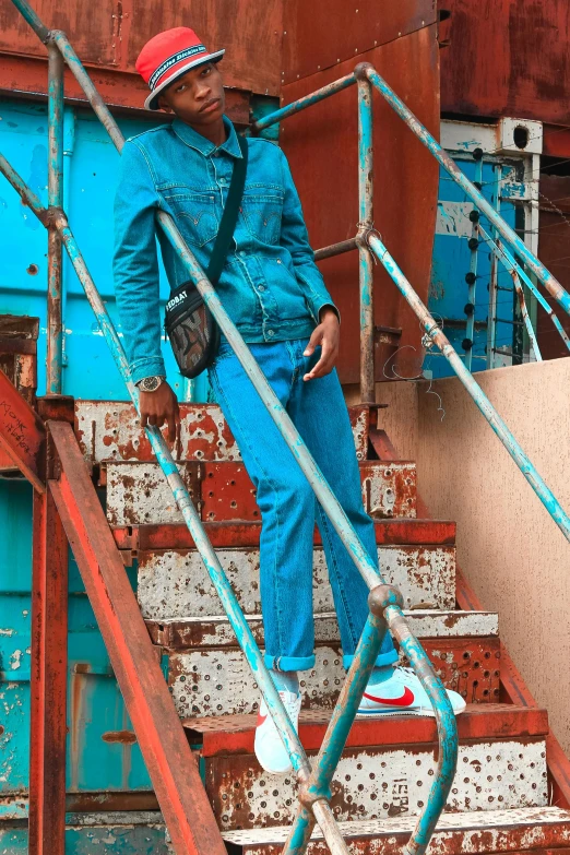 a man standing at the top of a set of stairs, an album cover, inspired by Afewerk Tekle, trending on pexels, teal uniform, blue long pants and red shoes, on ship, fashion shoot