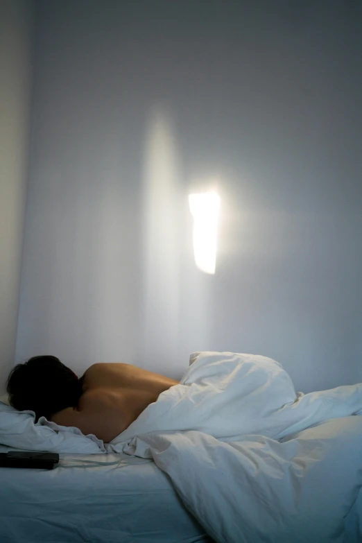 a man laying in bed next to a laptop computer, inspired by Nan Goldin, unsplash, romanticism, light ray, sun shafts, ignant, soft volumetric lights