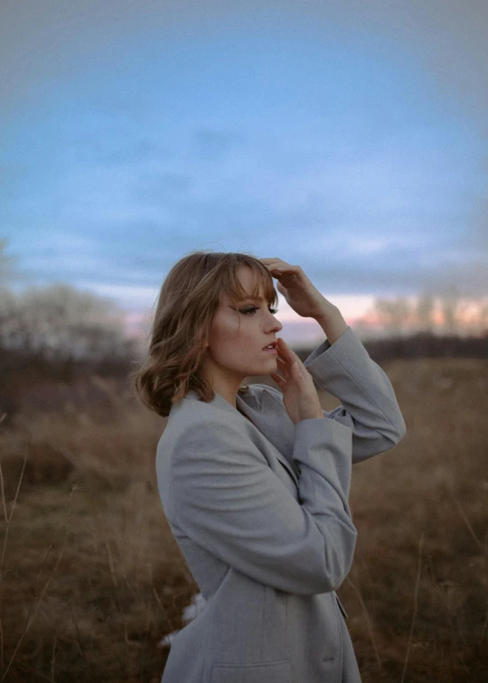 a woman in a gray coat standing in a field, an album cover, inspired by Elsa Bleda, pexels, realism, thoughtful ), profile image, concert, ansel ]