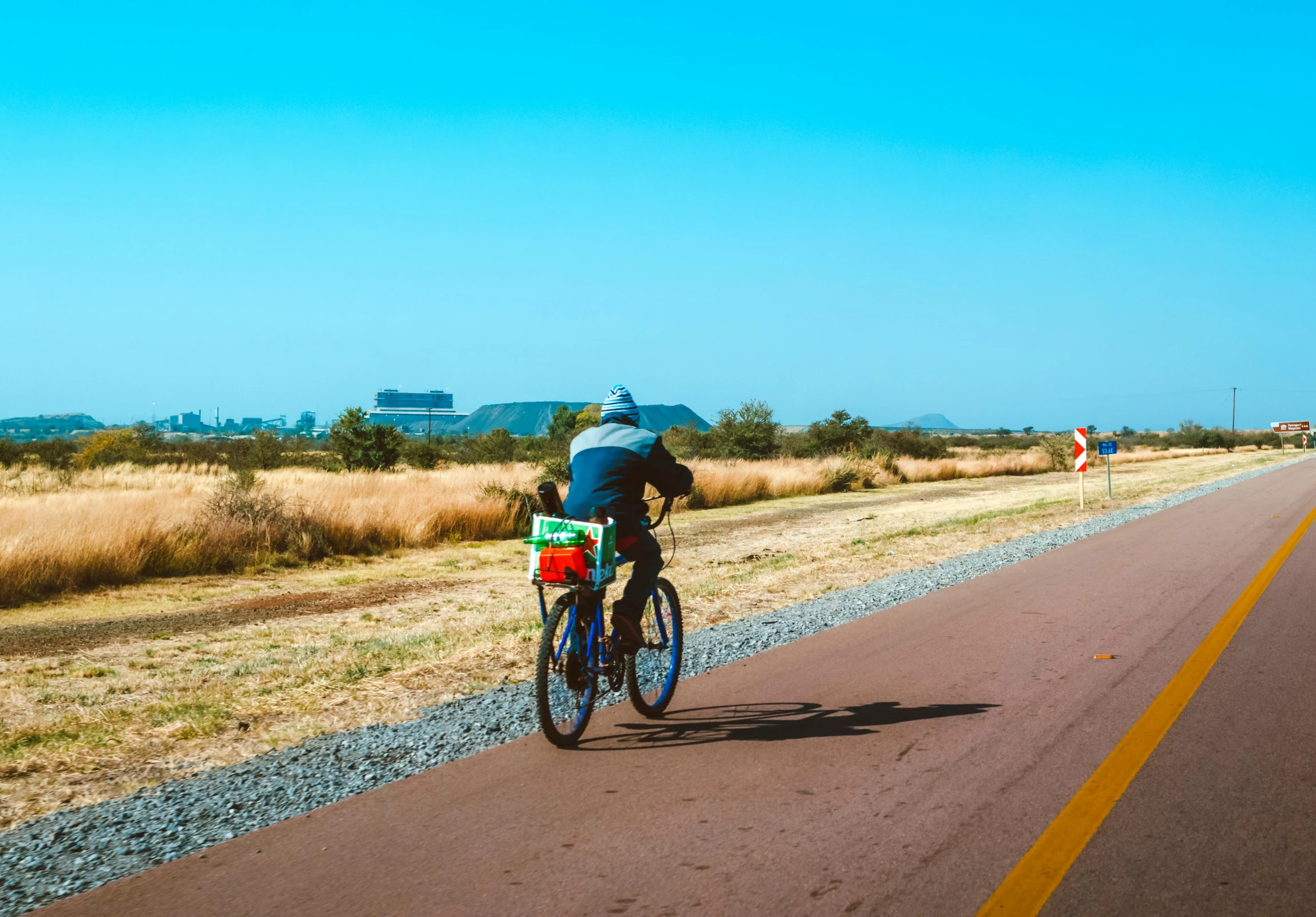 a person riding a bike down a road, pexels contest winner, african steppe, chartreuse and orange and cyan, hot weather, holiday season