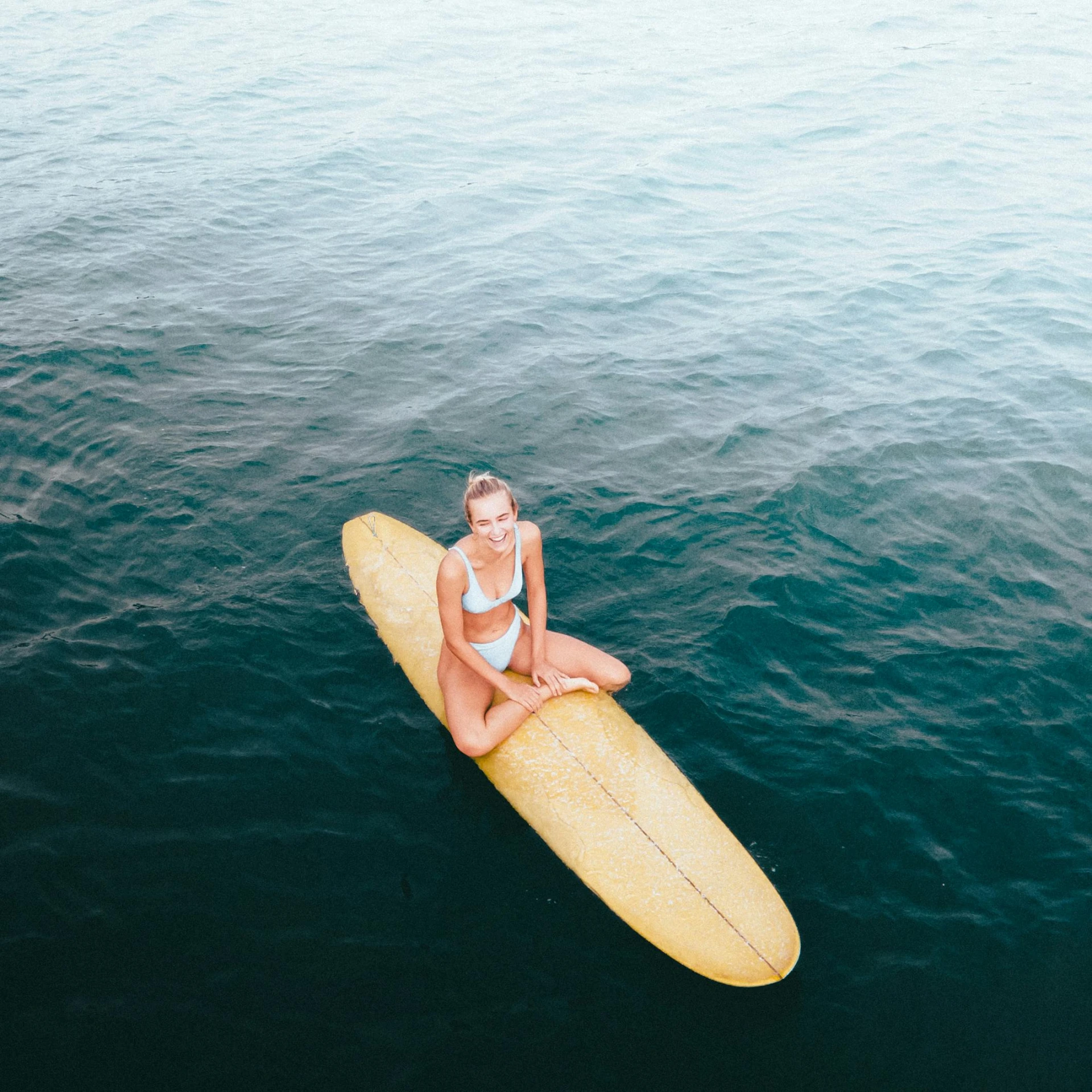 a woman sitting on a surfboard in the ocean, pexels contest winner, isolated, high angle, tan, confident looking