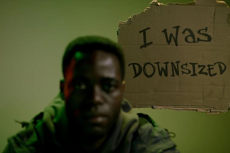a man holding a sign that says i was downloaded, by artist, pexels contest winner, dark-skinned, movie still of a tired, warfare, a person standing in front of a