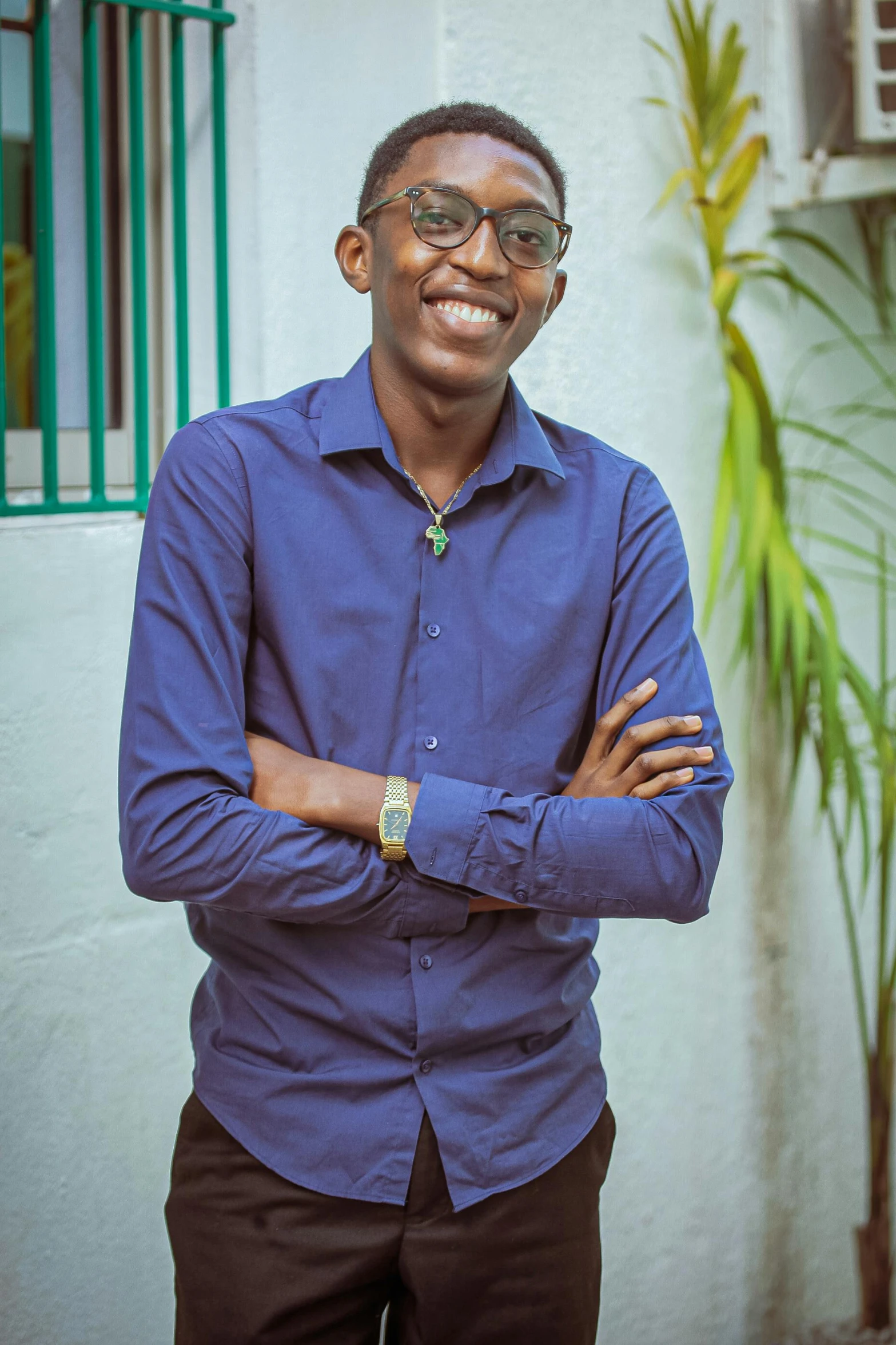 a man standing in front of a building with his arms crossed, inspired by Ibram Lassaw, pexels contest winner, cute slightly nerdy smile, ( ( dark skin ) ), he wears a blue shirt, young commoner