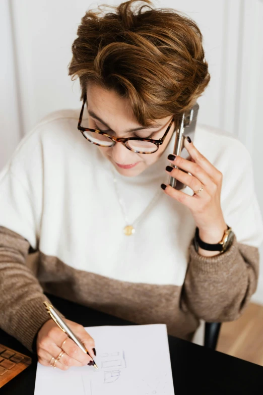 a woman sitting at a table talking on a cell phone, trending on pexels, brown and white color scheme, holding notebook, androgynous person, curated collections