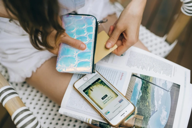 a woman sitting on a chair holding two cell phones, a picture, by Julia Pishtar, trending on pexels, holographic case display, flatlay book collection, at the beach, close up shot from the side