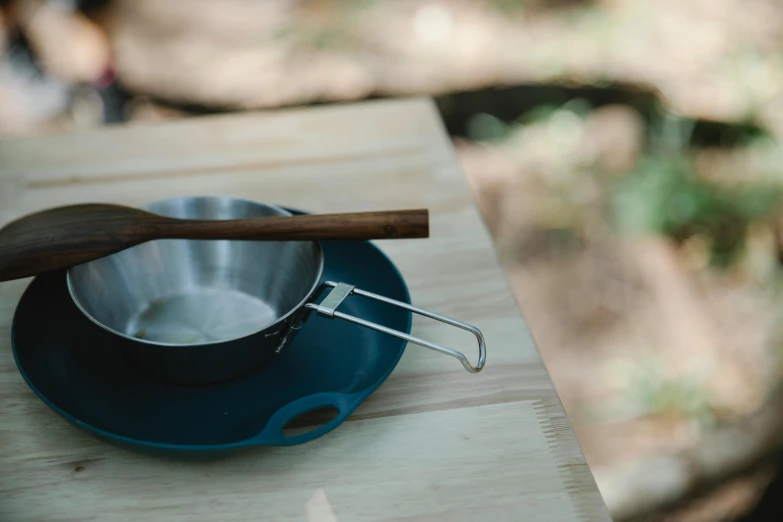 a pan sitting on top of a wooden table, unsplash, wilderness ground, blue, stainless steel, eucalyptus