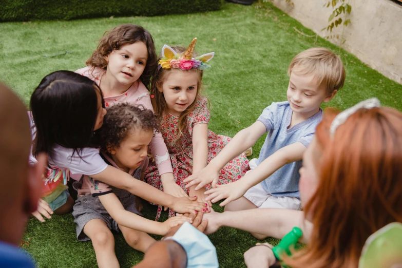 a group of children sitting on top of a lush green field, hands pressed together in bow, casual playrix games, mina petrovic, in the garden