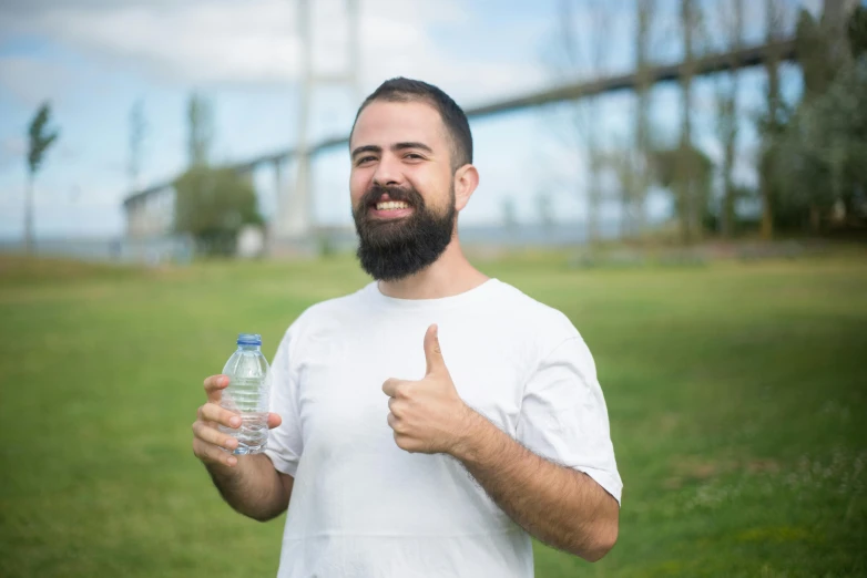 a man with a beard holding a bottle of water, giving a thumbs up to the camera, avatar image, joel torres, outdoor photo
