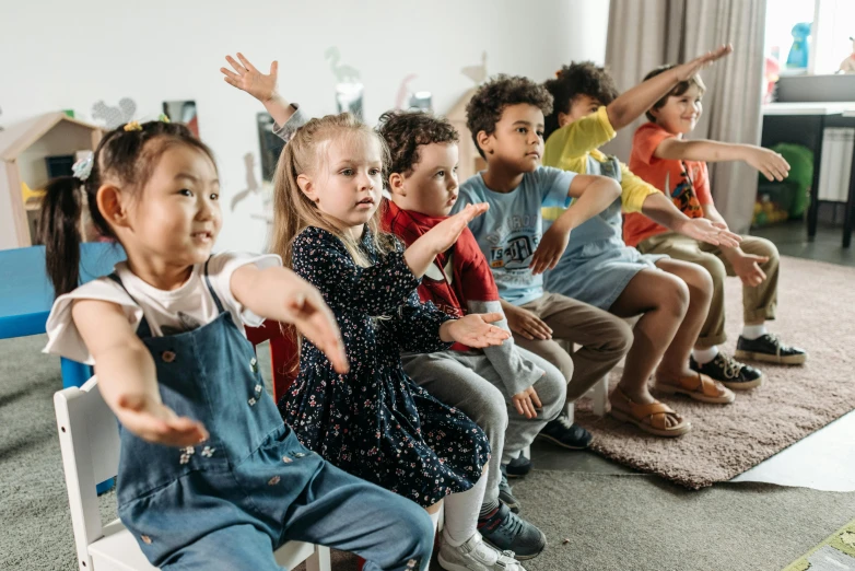 a group of children sitting on chairs in a room, arms out, profile image, colour photo, vibing to music