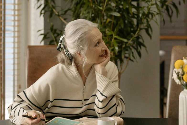 a woman sitting at a table with a cup of coffee, a portrait, trending on pexels, silver haired, pondering, wearing casual sweater, profile image