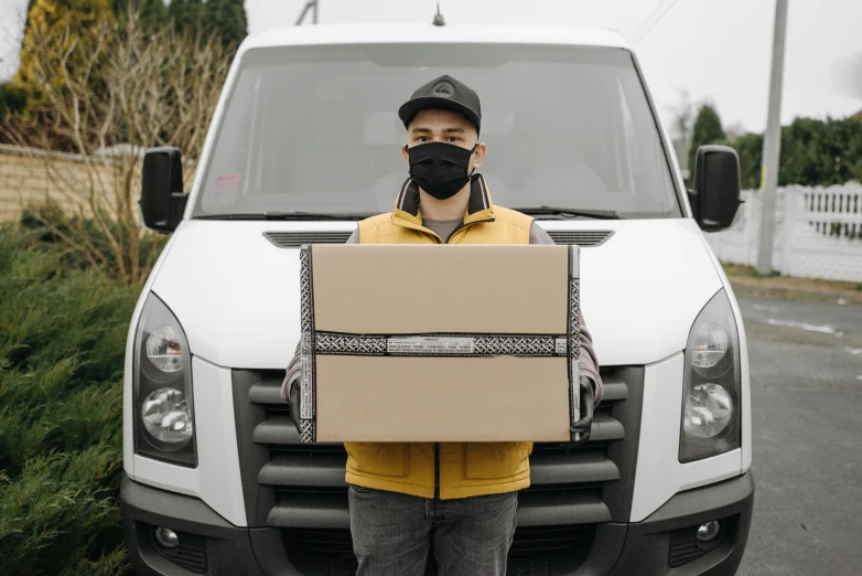 a man holding a box in front of a truck, pexels contest winner, renaissance, white man with black fabric mask, no - text no - logo, visor over face, as well as the handyboy