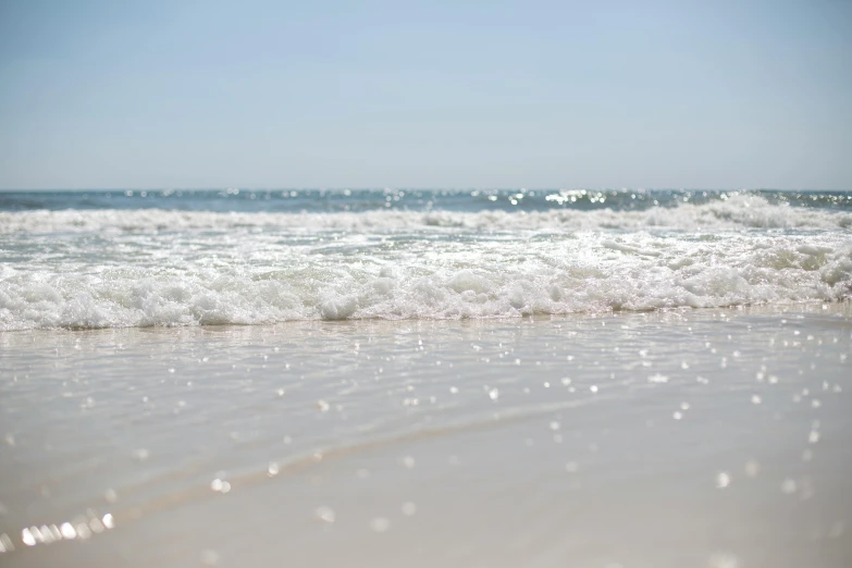a large body of water sitting on top of a sandy beach, a picture, sparkling water, up close, oceanside, afternoon
