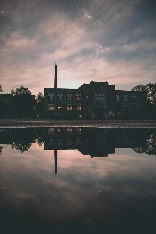 a reflection of a building in a puddle of water, a picture, unsplash contest winner, old lumber mill remains, twilight ; wide shot, college, tall factory