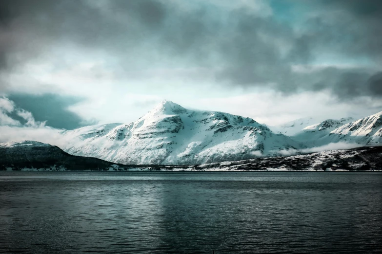 a large body of water with snow covered mountains in the background, by Þórarinn B. Þorláksson, pexels contest winner, hurufiyya, cold colors, desaturated, with snow on its peak, multiple stories