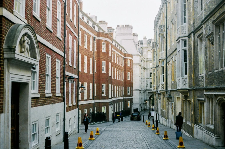 a group of people walking down a street next to tall buildings, unsplash, visual art, victorian england, cobblestone street, john pawson, 1999 photograph