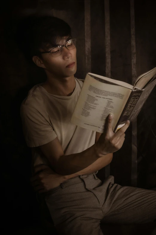 a man reading a book in a dark room, a portrait, inspired by Oliver Sin, pexels contest winner, photorealism, male ulzzang, in a dungeon, spectacled, ( ( theatrical ) )