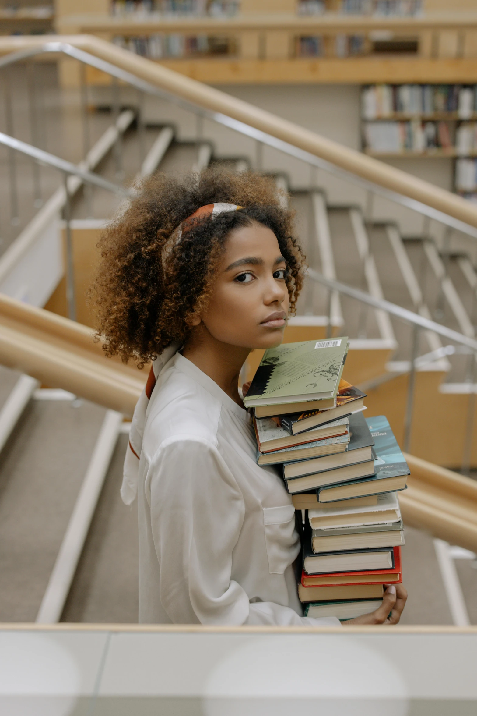 a woman holding a stack of books in a library, by Matija Jama, pexels contest winner, curly afro, movie still of a tired, with a backpack, handsome girl