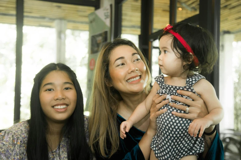 a woman holding a baby next to two women, inspired by Ruth Jên, pexels contest winner, hurufiyya, avatar image, asian descent, high quality upload, she is happy