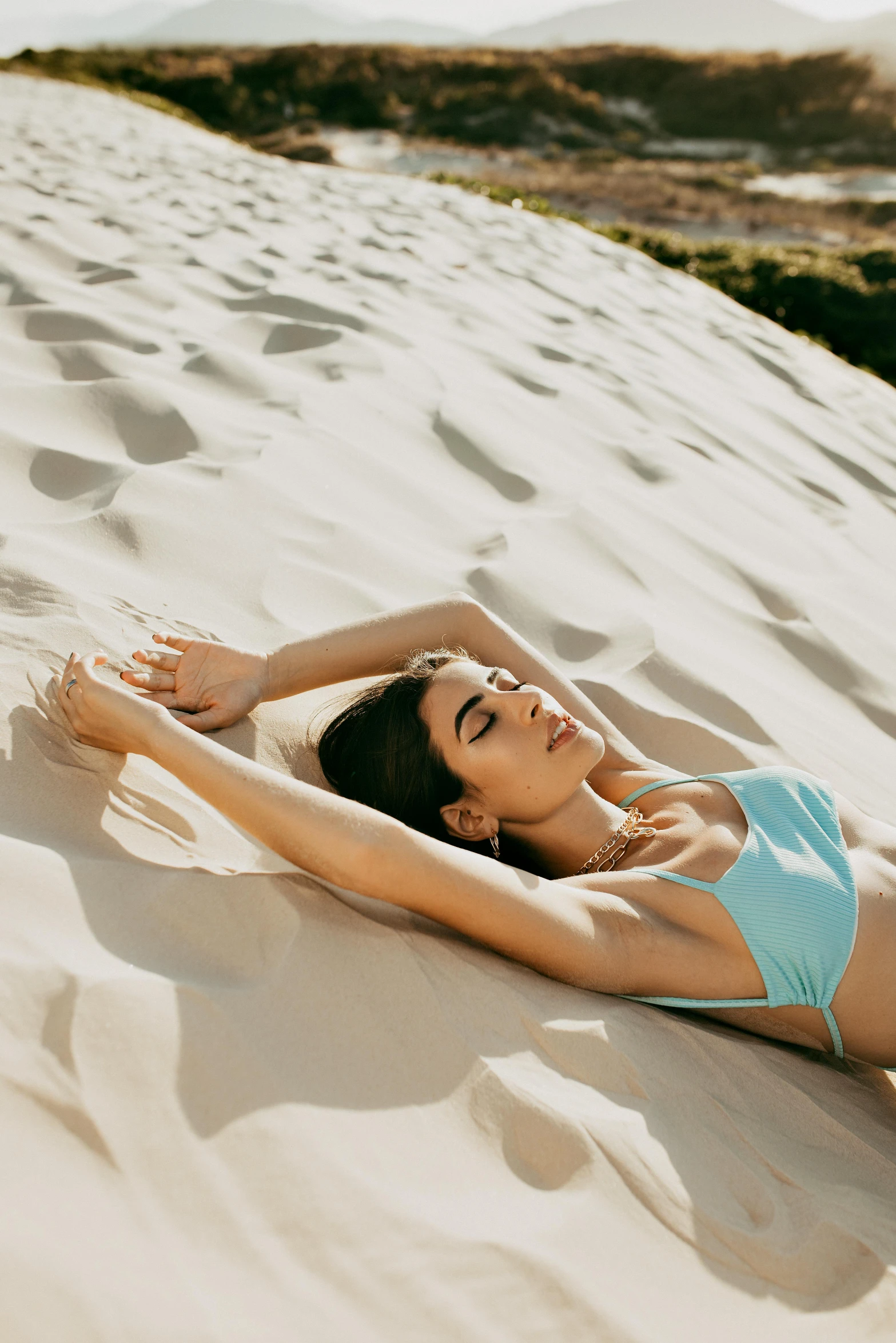 a woman laying on top of a sandy beach, trending on pexels, dune style, perfectly shaded body, blue, dua lipa