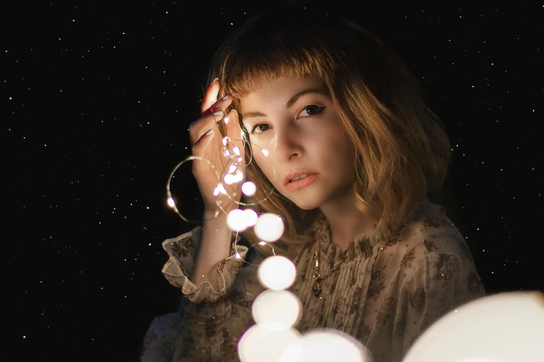 a woman holding a string of lights in front of her face, an album cover, trending on pexels, magical realism, sophia lillis, hanging out with orbs, anna nikonova aka newmilky, thoughtful