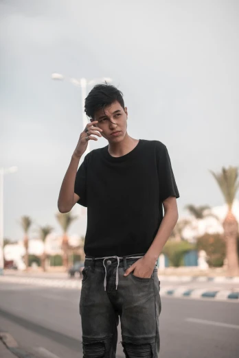 a man standing on the side of a road talking on a cell phone, by Ahmed Yacoubi, wearing a black!! t - shirt, beautiful androgynous girl, boy has short black hair, posing for a picture