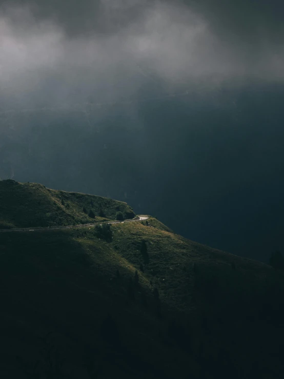 a house sitting on top of a hill under a cloudy sky, unsplash contest winner, dark moody backlighting, rain and light fog, in the swiss alps, dramatic lighting from above