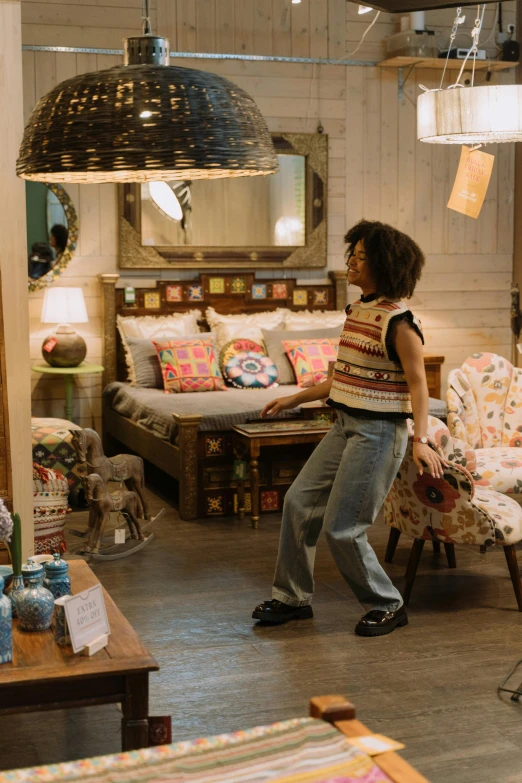 a woman standing in a living room next to a couch, maximalism, official store photo, upcycled, early evening, walking down