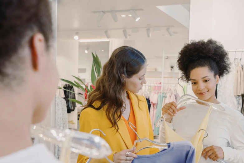 two women looking at a t - shirt in a store, trending on pexels, lady using yellow dress, looking into a mirror, wearing a fancy jacket, thumbnail