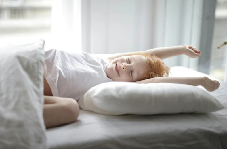 a little girl laying on top of a bed, pexels contest winner, happening, young redhead girl in motion, white pillows, winking, very comfy]